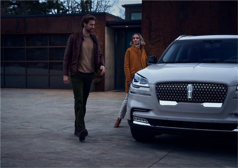A man and a woman approaching a 2023 Lincoln Aviator® SUV, which illuminates certain lights when they are close | Seekins Lincoln in Fairbanks AK