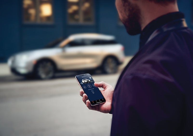 A person is shown interacting with a smartphone to connect to a Lincoln vehicle across the street. | Seekins Lincoln in Fairbanks AK