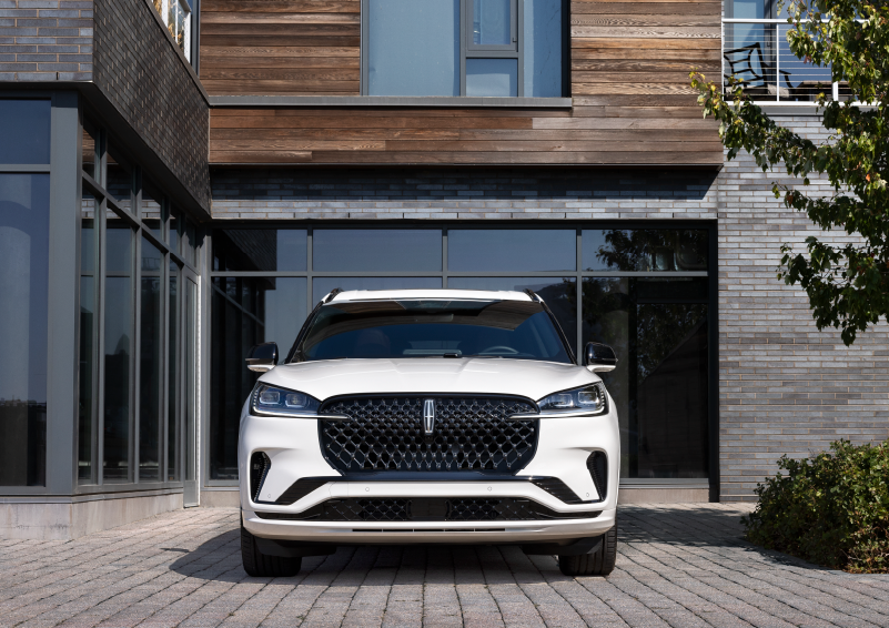 A white 2025 Lincoln Aviator® SUV is shown parked outside a modern building with gray brick and wood accents. | Seekins Lincoln in Fairbanks AK