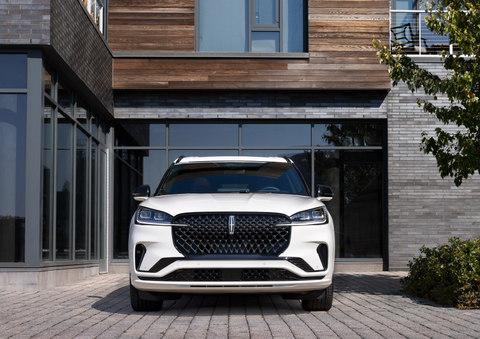 A white 2025 Lincoln Aviator® SUV is shown parked outside a modern building with gray brick and wood accents. | Seekins Lincoln in Fairbanks AK