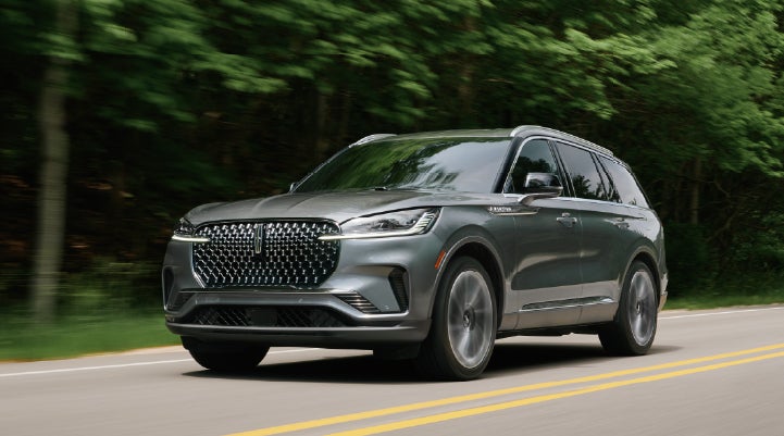A 2027 Lincoln Aviator® SUV is being driven down a road lined with trees. | Seekins Lincoln in Fairbanks AK